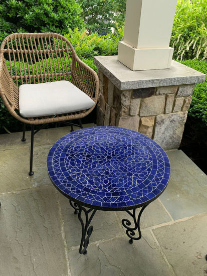 A wicker chair beside a vibrant blue mosaic table on a patio, showcasing Moroccan craftsmanship and mid-century design.