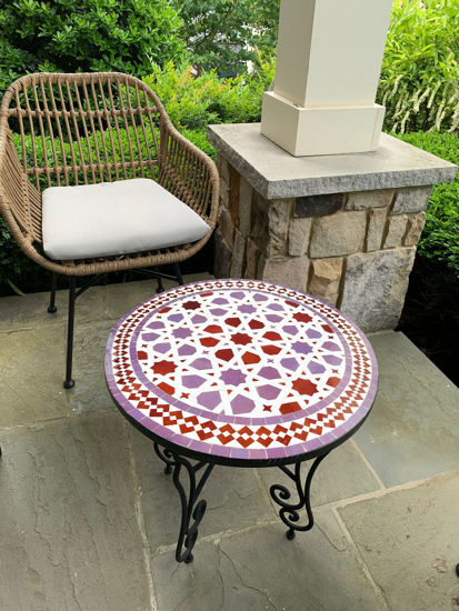 Wicker chair and a colorful purple and pink mosaic table on a patio, showcasing Moroccan craftsmanship and design.