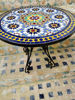 A handmade Moroccan mosaic table with colorful tiles sits on a patio, blending traditional artistry with modern decor aesthetics.