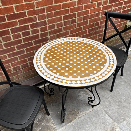 A gold and white handmade round mosaic coffee table with two chairs on a patio, showcasing Moroccan craftsmanship and elegance.