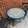 A handmade Moroccan mosaic coffee table with two chairs on a patio, showcasing intricate tile work and vibrant colors.