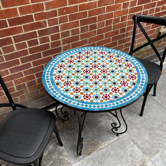 A handmade Moroccan mosaic coffee table with two chairs on a patio, showcasing intricate tile work and vibrant colors.