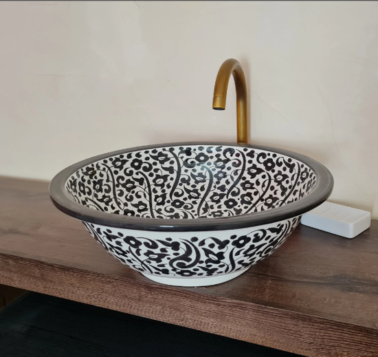 Black and white ceramic wash basin with a gold faucet, showcasing Moroccan craftsmanship and elegant design for bathrooms.