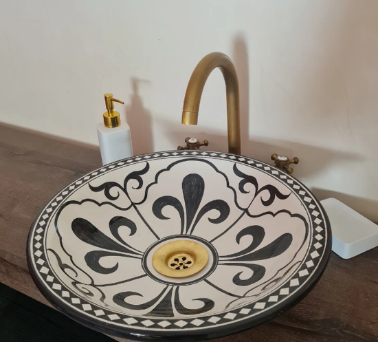 Black and white ceramic bathroom sink with a gold faucet, showcasing traditional Moroccan design and craftsmanship.