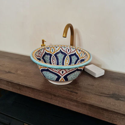 Colorful handmade Moroccan ceramic bowl on a wooden counter, showcasing intricate patterns and vibrant Mediterranean design.