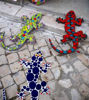 Three colorful mosaic geckos made of ceramic tiles, each with unique designs, arranged on the ground in a vibrant display.
