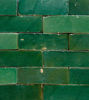 A wall covered in vibrant emerald green ceramic tiles, handcrafted in Morocco, highlighting their unique artisanal quality.