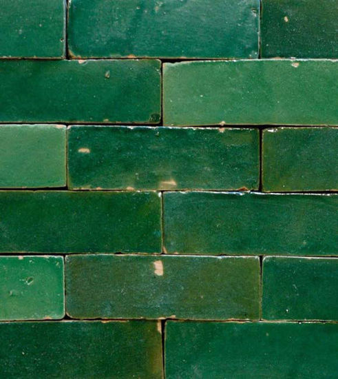 A wall covered in vibrant emerald green ceramic tiles, handcrafted in Morocco, highlighting their unique artisanal quality.
