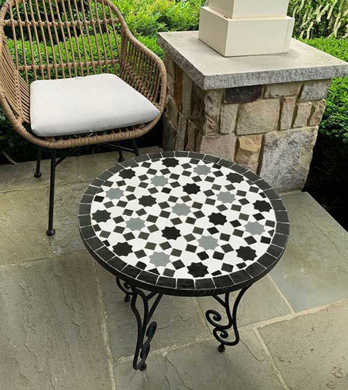 Round black and white mosaic table on a patio, featuring handcrafted Moroccan Zellige tiles that enhance outdoor decor.