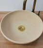 A round white ceramic vessel sink topped with a brass faucet, showcasing intricate Moroccan patterns and a neutral patina finish.