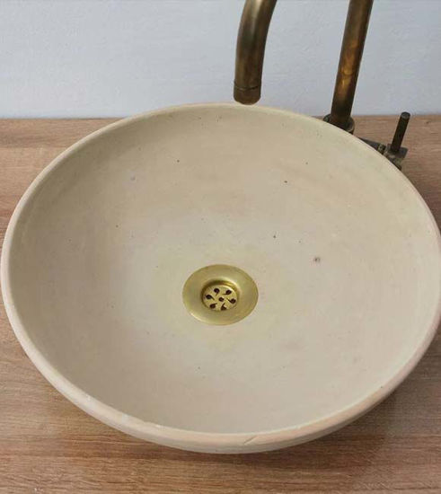A round white ceramic vessel sink topped with a brass faucet, showcasing intricate Moroccan patterns and a neutral patina finish.