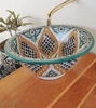 A decorative, artisan-crafted Moroccan ceramic sink resting on a table, adorned with vivid colors and intricate patterns.