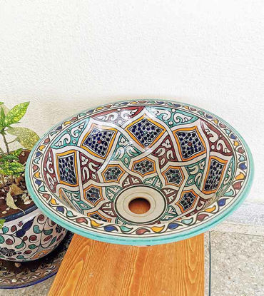 Colorful handpainted Moroccan ceramic sink bowl on a wooden table, showcasing intricate designs and vibrant motifs.