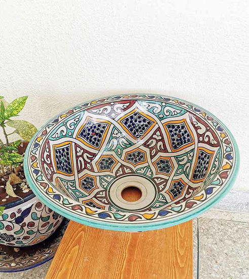 Colorful handpainted Moroccan ceramic sink bowl on a wooden table, showcasing intricate designs and vibrant motifs.