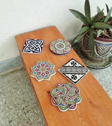 Four handmade Moroccan ceramic coasters displayed on a wooden table, showcasing intricate hand-painted designs and textures.