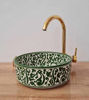A decorative green and gold bowl-shaped sink with a gold faucet, exemplifying handcrafted Moroccan style and intricate detailing.