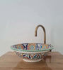 Unique handmade Moroccan ceramic bowl with rich colors and patterns, complemented by a stylish brass faucet for modern spaces.