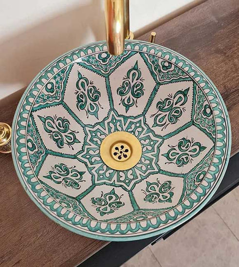 A handcrafted mint green Moroccan ceramic sink rests on a wooden counter, showcasing intricate patterns and mid-century modern style.