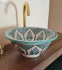 A mint green ceramic washbasin with traditional Moroccan designs sits atop a wooden counter, highlighting its handcrafted artistry.