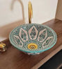 A unique mint green Moroccan ceramic sink is displayed on a wooden counter, featuring elegant patterns and mid-century modern aesthetics.
