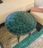Round emerald green mosaic table on a green tile floor, showcasing intricate patterns and handcrafted Moroccan design.