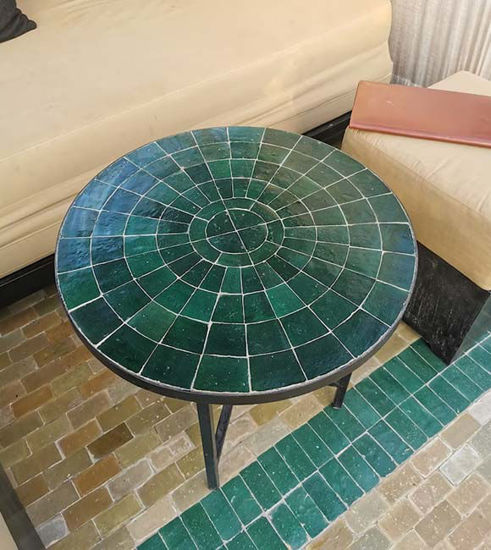 Round emerald green mosaic table on a green tile floor, showcasing intricate patterns and handcrafted Moroccan design.