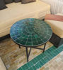 Handmade round emerald green mosaic table on a green tile floor, featuring mid-century patterns and artisan craftsmanship.