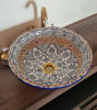 Decorative round ceramic sink with intricate fish scale patterns and brass rim, placed on a wooden counter.