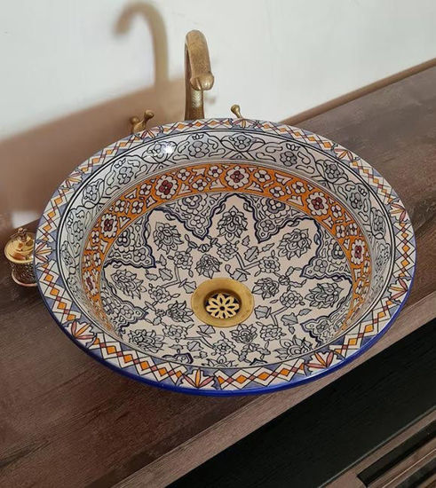 Decorative round ceramic sink with intricate fish scale patterns and brass rim, placed on a wooden counter.