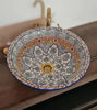 Artisan-crafted round sink with detailed fish scale patterns and polished brass rim, resting on a wooden counter surface.