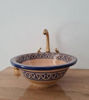 Terracotta ceramic bathroom sink with hand-painted Moroccan patterns and brass faucet on a wooden countertop.