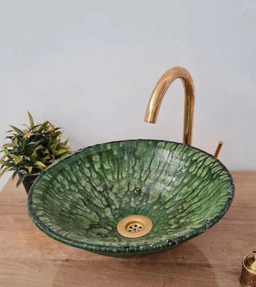A rustic green bowl-shaped sink with a gold faucet is displayed on a wooden table, highlighting its Moroccan motif.