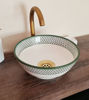 A white and green ceramic bowl with a fish scales design rests on a wooden counter, showcasing Moroccan artistry.