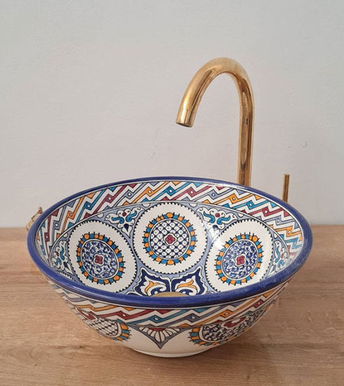 A handcrafted Moroccan vessel sink with a gold faucet and intricate blue and white patterns, showcasing unique artisan design.