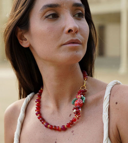 A woman wearing a red beaded bracelet adorned with a pomegranate charm, perfect for adding a fun touch to your jewelry collection.