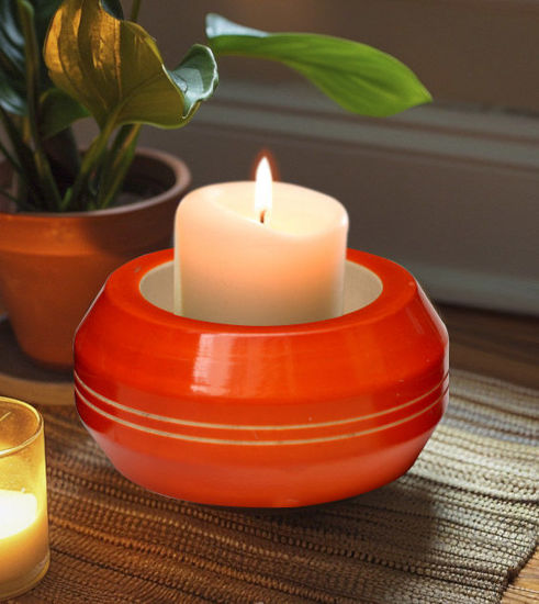 A candle placed on a red bowl, showcasing a handcrafted wooden tea light holder from Channapatna, India.