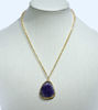 Handmade raw amethyst pendant necklace on a gold chain, featuring a striking purple stone with organic texture and shine.