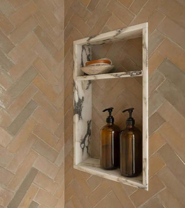 A bathroom featuring a shelf with two shampoo bottles, accented by honey beige handmade Moroccan Zellige tiles.