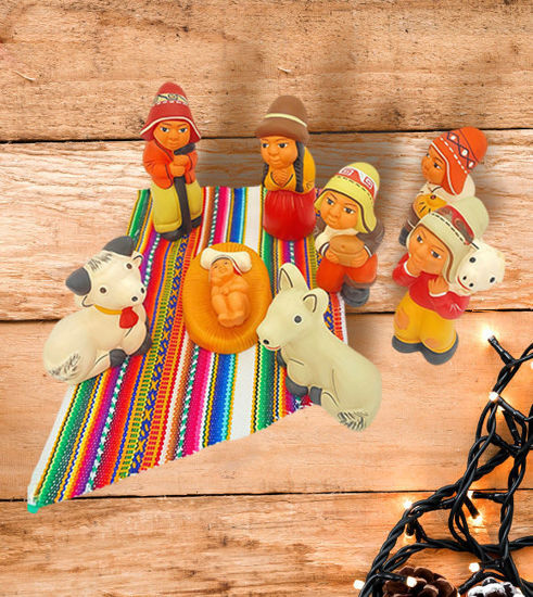 A wooden table displays a handcrafted Peruvian nativity scene ornament set, featuring the Holy Family in vibrant folk art style.