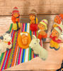 A wooden table showcases a colorful nativity scene ornament set, handcrafted in Peru, depicting the Holy Family in folk art design.