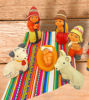On a wooden table, a Peruvian nativity scene ornament set is arranged, highlighting the Holy Family with intricate hand-painted details.