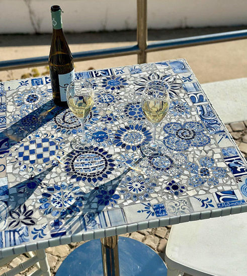 Blue and white floral mosaic tabletop with wine glasses, showcasing handcrafted Portuguese tile art for indoor or outdoor use.